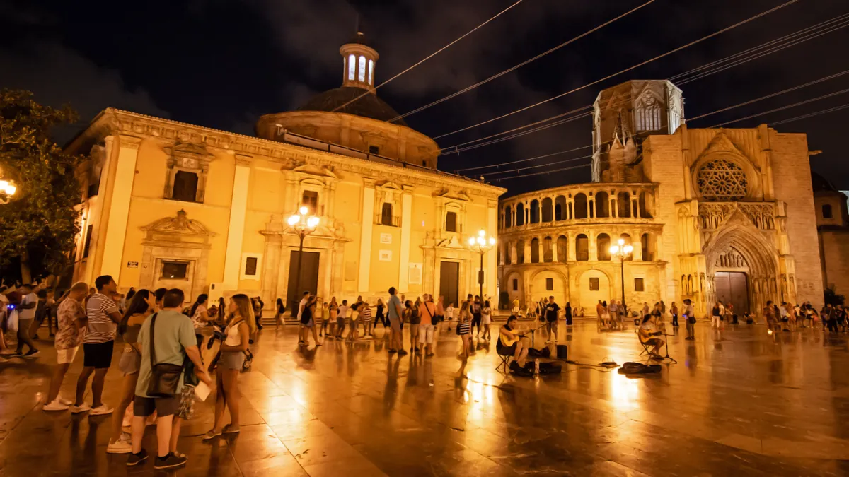 Plaza de la Virgen ve Valencii v noci, s osvětlenými dveřmi katedrály a fontánou na náměstí