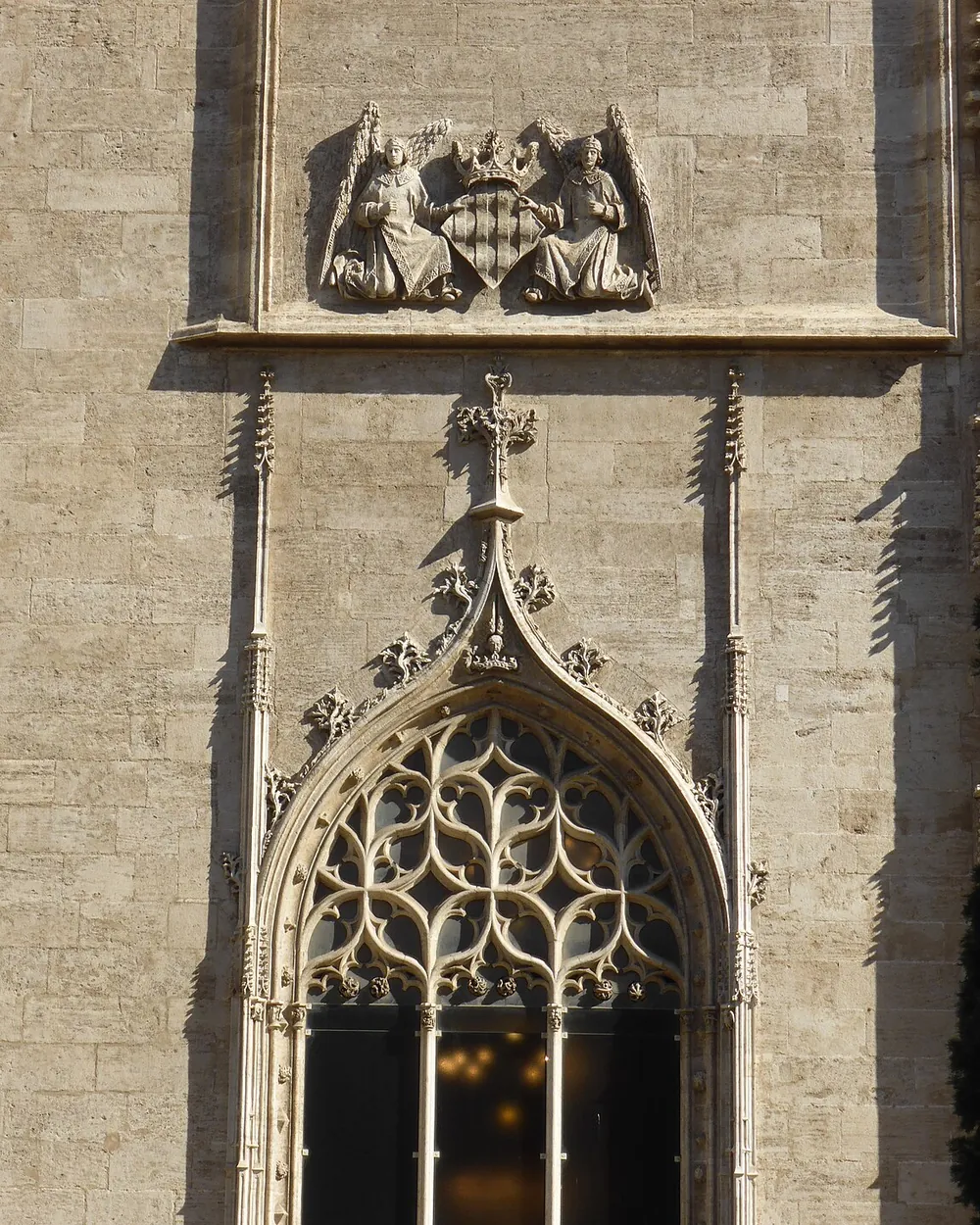 Et gotisk sprossevindue og et udskåret våbenskjold på stenfacaden af Lonja de la Seda i Valencia, med en gadelampe ved siden af