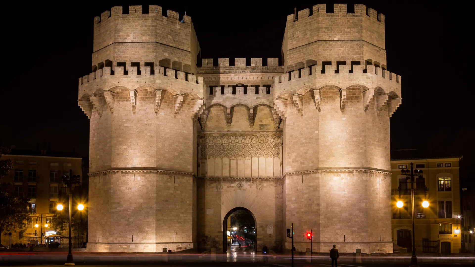 De to krenelerede tårne på Torres de Serranos i Valencia, oplyst i varm sten mod en sort nattehimmel